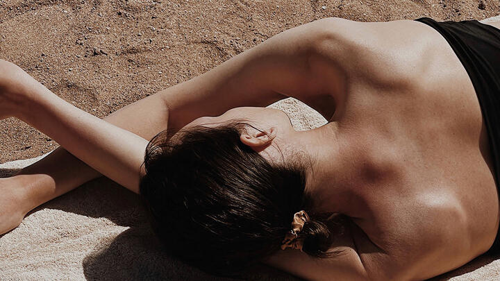 Woman in black swimsuit lying sideways on a towel on a sandy beach